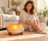 Woman seated on a rug beside a glowing Himalayan salt foot dome on a wooden stand.